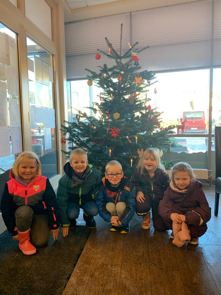 Kinder sitzen vor einem geschmückten Tannenbaum